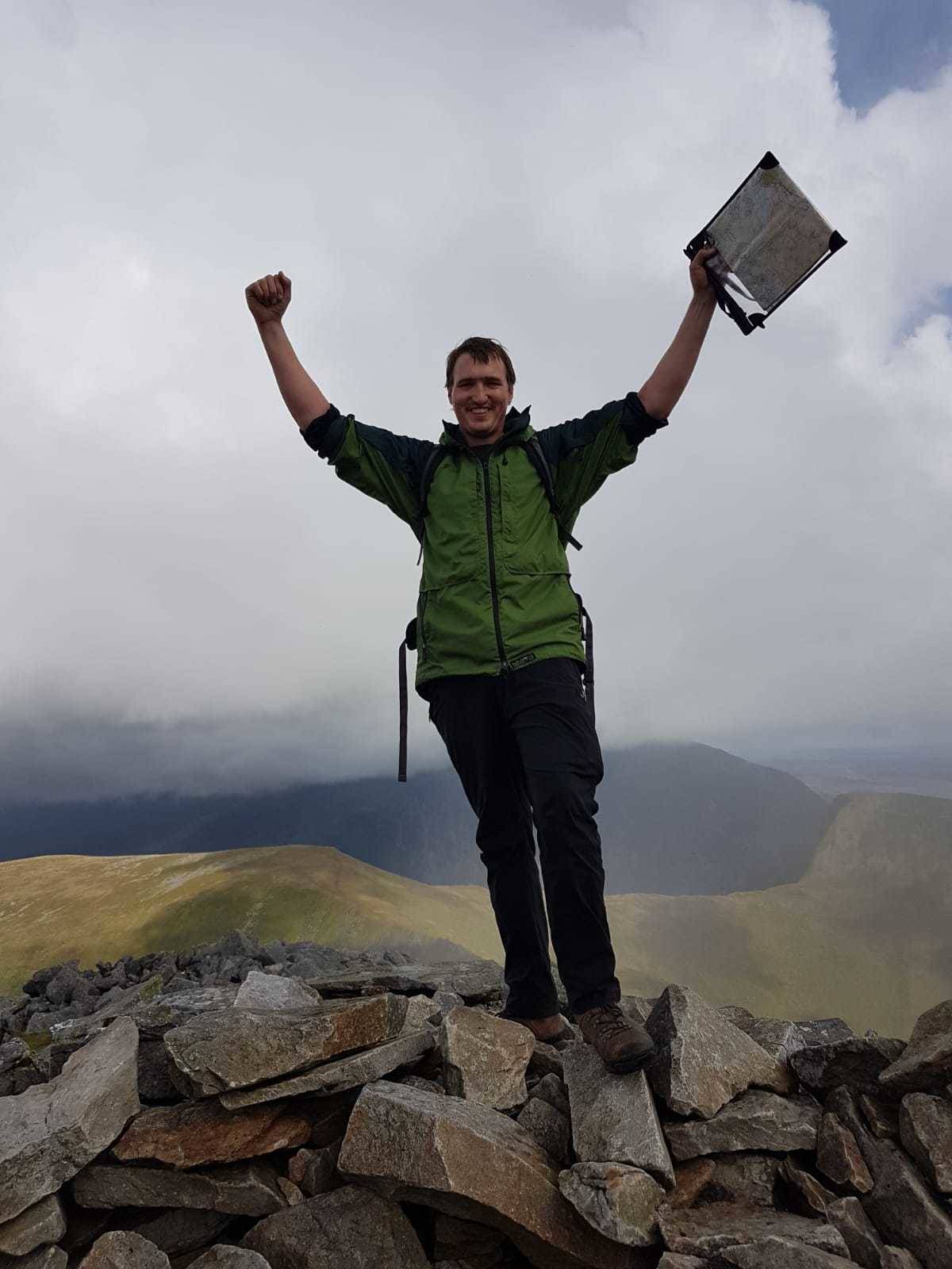 A photograph of a man standing at the top of a mountain with a map in his hand