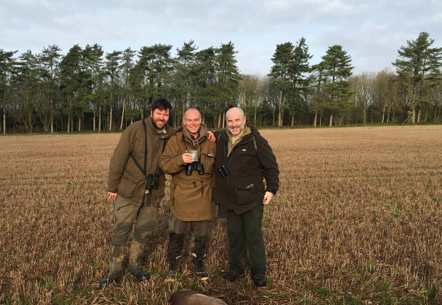 A photograph of three men in a field with hunting equipment