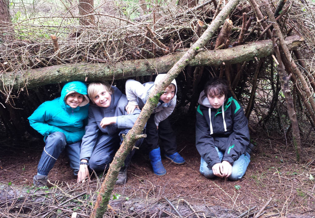 A photograph of 4 children under a shelter in the woods