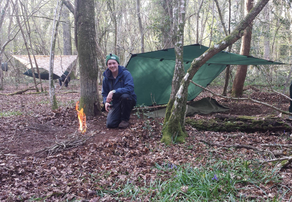 A man making an outdoor camping shelter in the woods.
