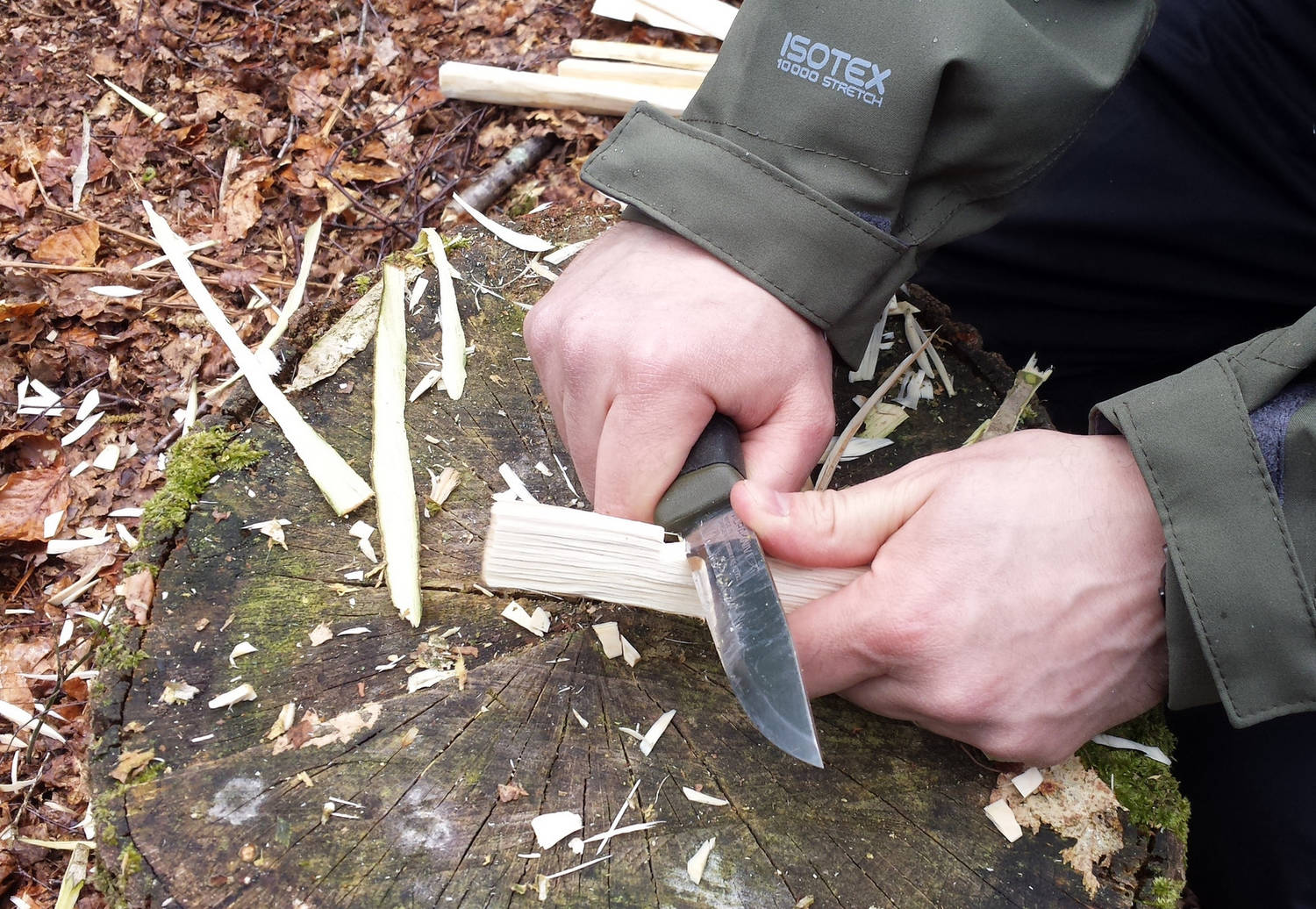 Somebody carving a piece of wood with a knife in the woods