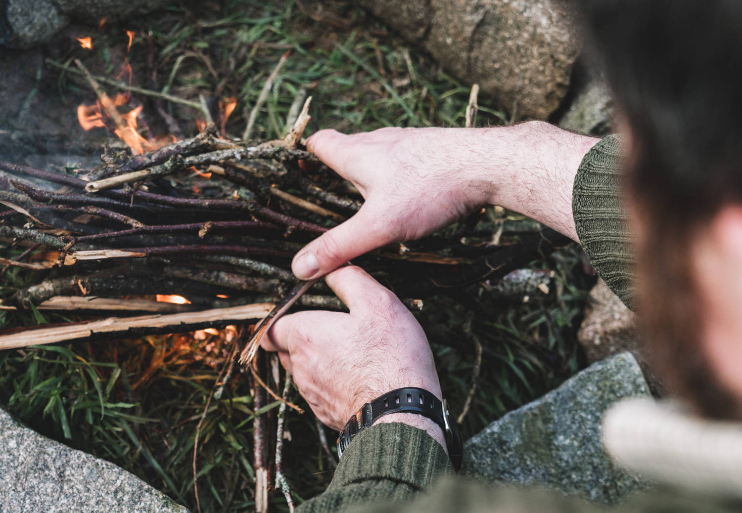 A man holing twigs over a lit fire