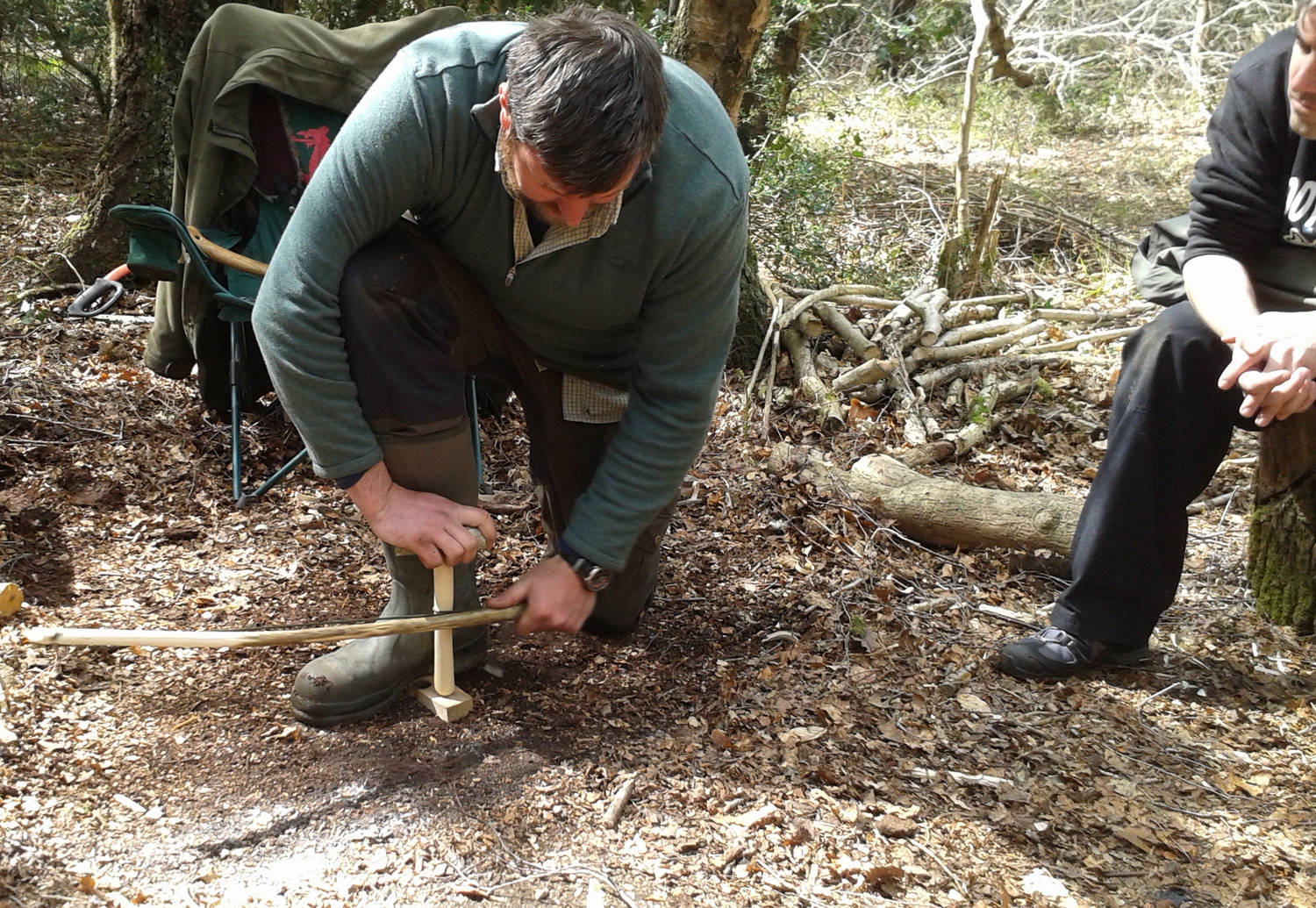 A photograph of a man lighting a fire with wood and a fire lighter in the woods.