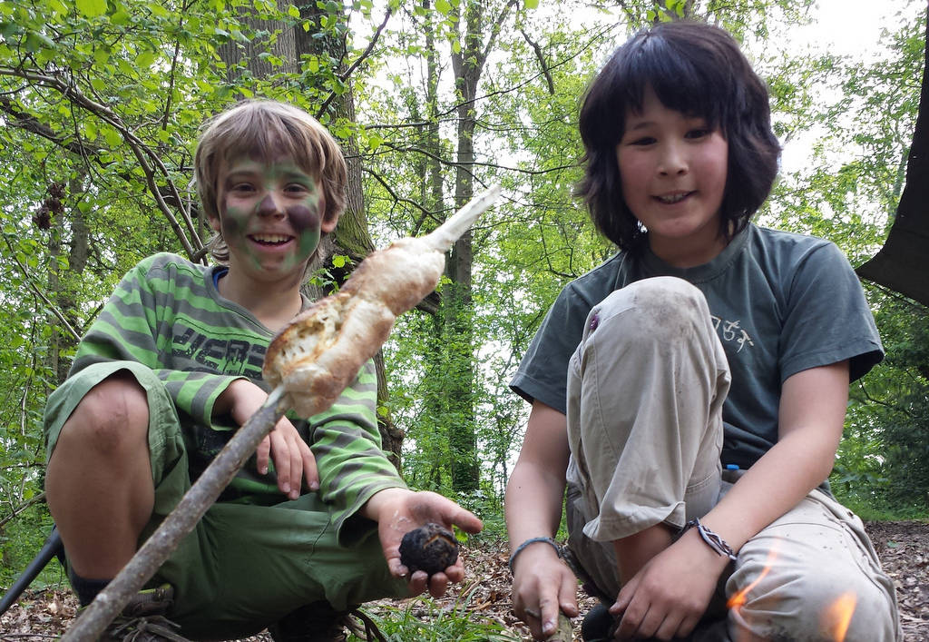 A photograph of two children cooking over a fire in the woods