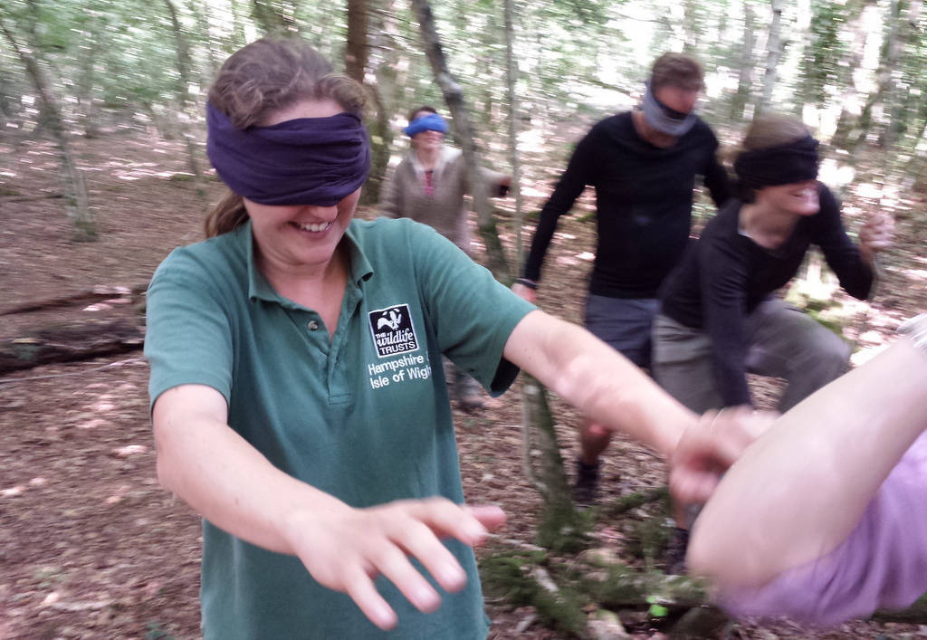 A photograph of a blindfolded woman playing game and smiling in the woods